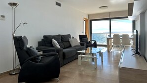 A modern living room with a sofa, armchairs, a coffee table, and a view of the sea.