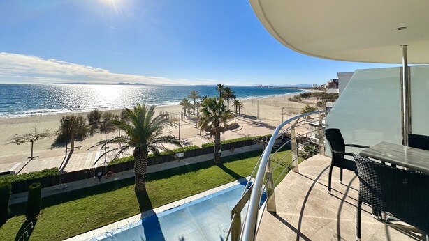 A balcony with a view of the beach and ocean, a pool, and outdoor furniture.