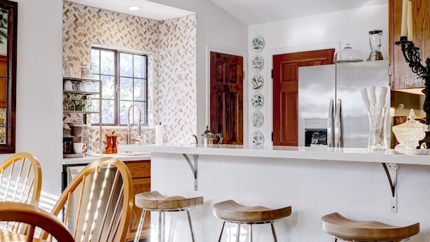 Une cuisine moderne avec des tabourets de bar en bois, un comptoir blanc et un réfrigérateur.