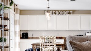 Une cuisine moderne avec des meubles blancs, un coin repas avec des chaises en bois et une table, et un salon avec un canapé et un tapis.