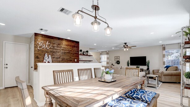 Une cuisine moderne avec un mur d’accent en bois, un coin repas avec une table et des bancs en bois, et un salon avec un canapé et un téléviseur.