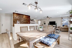 Una cocina moderna con un revestimiento de madera, un comedor con una mesa y bancos de madera, y una sala de estar con sofá y televisor.