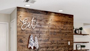 Une cuisine moderne avec un mur d’accent en bois, un plan de travail blanc et un panneau indiquant « On mange ici ».