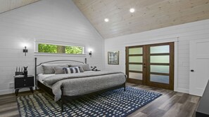 Quarto com cama, mesas de cabeceira, janela e porta com painéis de vidro jateado.