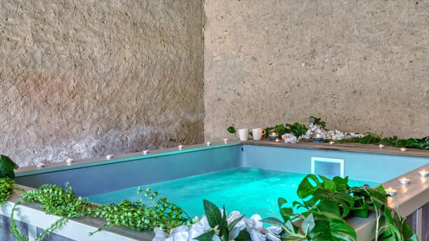 Une piscine rectangulaire à l’eau claire, entourée de verdure et illuminée de bougies.