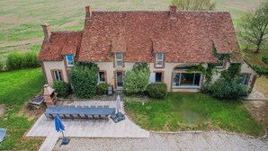 Une grande maison avec un toit en tuiles, un porche à l’avant et un patio aménagé avec du mobilier d’extérieur.