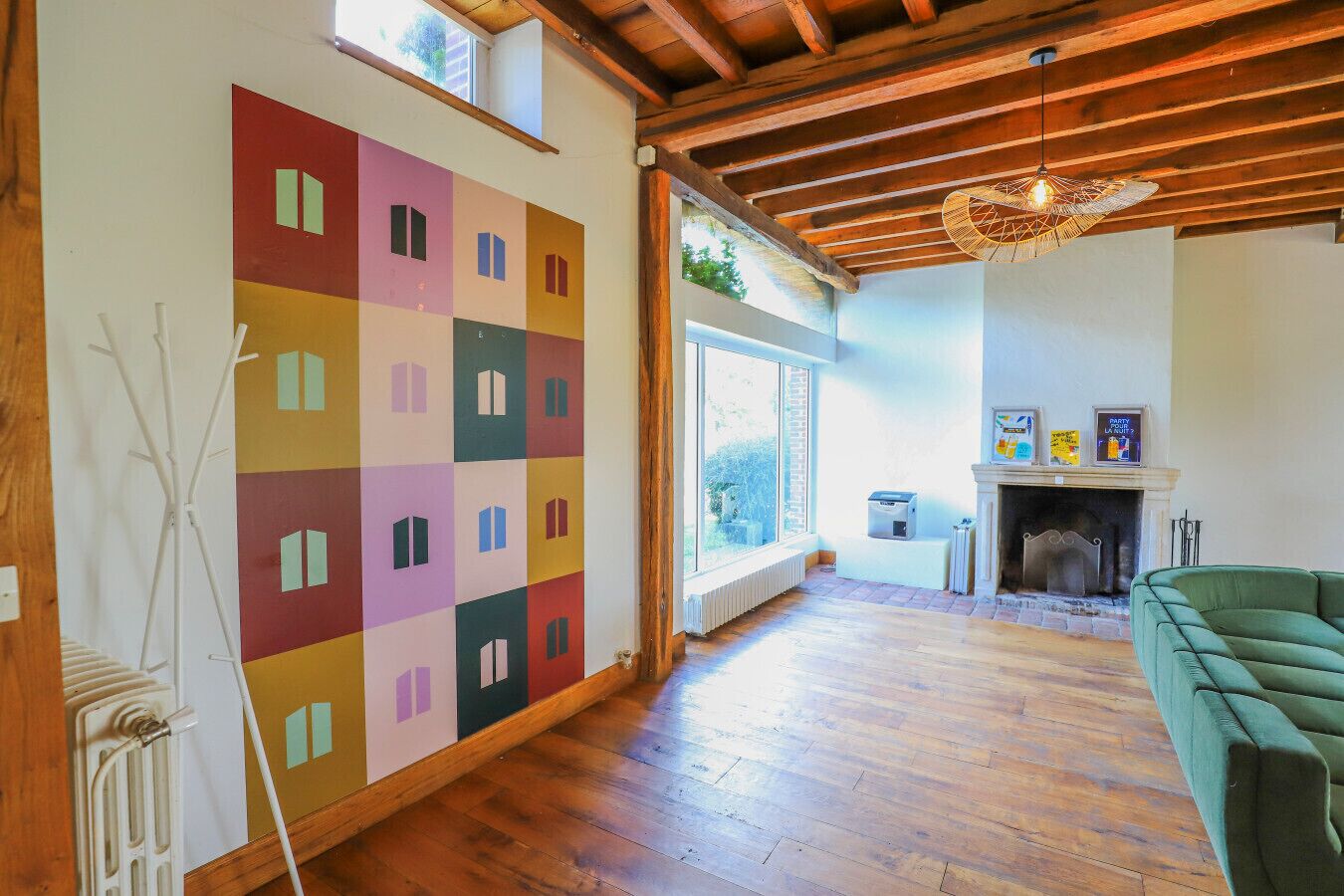 Un salon spacieux doté d’une grande fenêtre, d’un parquet, d’un canapé vert et d’une œuvre d’art murale abstraite aux couleurs vives.