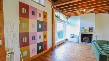 Un salon spacieux doté d’une grande fenêtre, d’un parquet, d’un canapé vert et d’une œuvre d’art murale abstraite aux couleurs vives.