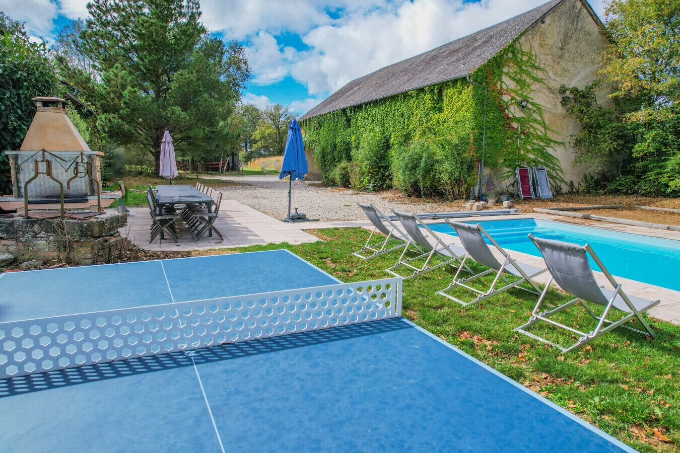 An outdoor pool area with lounge chairs, a ping pong table, and a rustic building with ivy.
