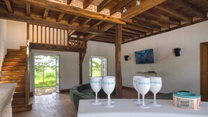 Un intérieur rustique avec un escalier en bois, un coin salon avec des coussins verts et une table sur laquelle on trouve des verres à vin et une boîte à café.