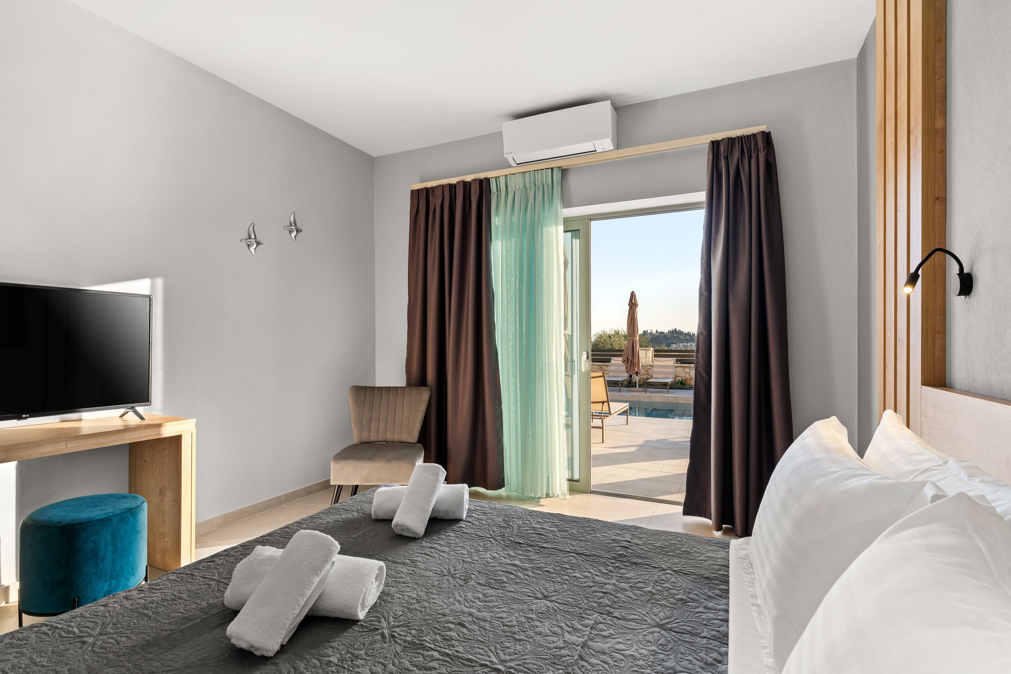 Hotellihuone, jossa on sänky, työpöytä, jossa on televisio, tuoli ja näkymä ulos.