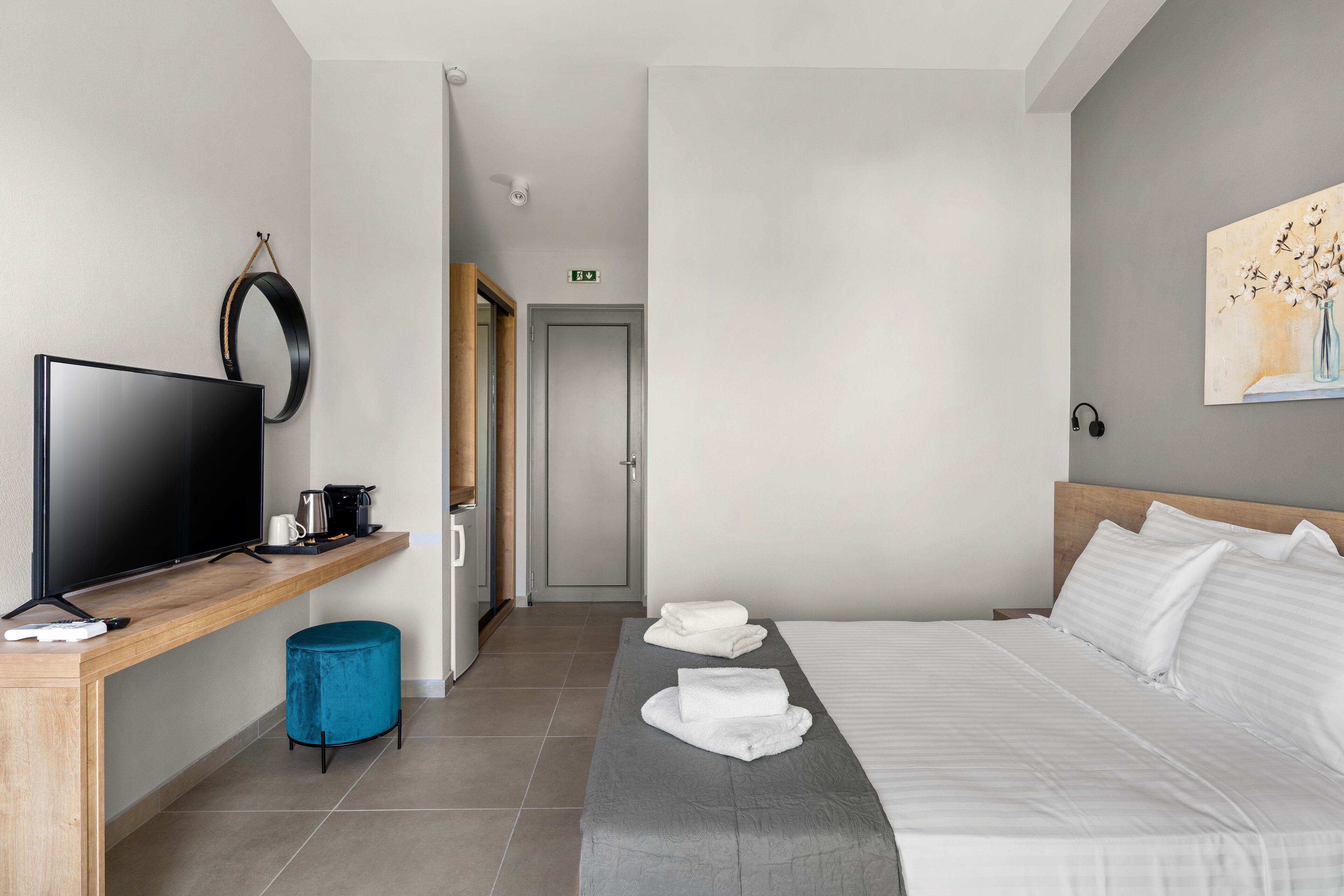 A hotel room with a bed, a TV, a desk with a coffee maker, and a painting on the wall.