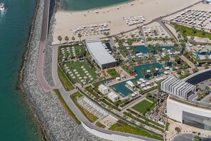 An aerial view of a resort with a beach, a pool area, and a rocky shoreline. - HiGuests - EMAAR 52-42 (Dubai)