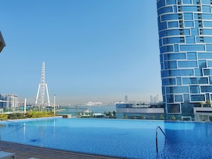 Un hôtel moderne doté d’une grande piscine à débordement, avec une grande roue en arrière-plan et une vue sur les gratte-ciel de la ville.