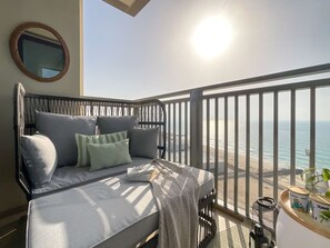 A balcony with a bed, pillows, and a view of the beach. - HiGuests - EMAAR 52-42 (Dubai)