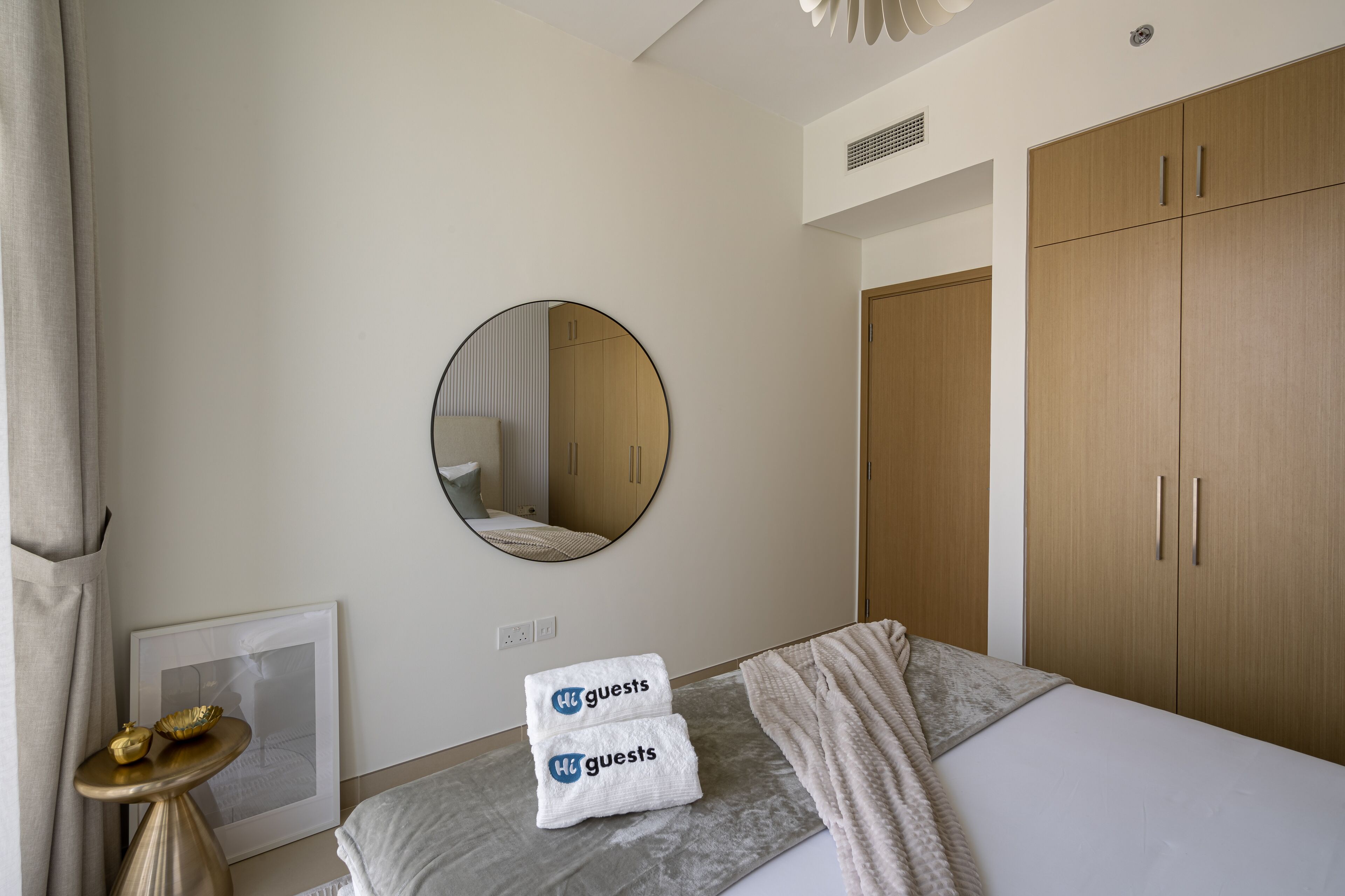 Habitación de hotel con cama, un espejo redondo, un armario y una mesita con toallas.