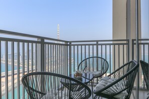 A balcony with two wicker chairs, a glass table with a decorative item, and a view of a coastal cityscape. - HiGuests - EMAAR 52-42 (Dubai)