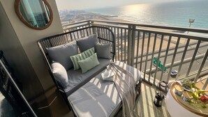 Un balcon avec un canapé, un miroir rond et une vue sur la plage et le paysage urbain.