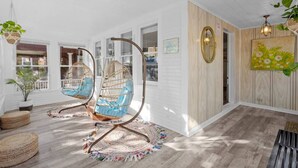 Une pièce spacieuse avec une grande fenêtre, un fauteuil suspendu, un plancher en bois et un miroir décoratif.