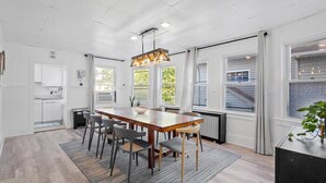Une cuisine moderne avec des meubles blancs, une table à manger en bois et un luminaire suspendu.