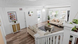 Un salon spacieux avec une balustrade blanche, un canapé beige, une table basse et une grande fenêtre laissant entrer la lumière naturelle.