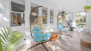 Une pièce lumineuse avec de grandes fenêtres, deux fauteuils suspendus dotés de coussins bleus et un plancher en bois.