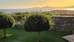A garden with a stone wall, a small tree, and a view of the sea and distant hills. - Paros Afrodite Luxury Villas with private pool & spa max 12 persons (ΑΓΚΑΙΡΙΑ ΠΑΡΟΥ)