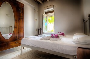 Ein Schlafzimmer mit einem Bett, einer Holzkombination, einem Spiegel und einem Fenster mit Blick auf Grünflächen.