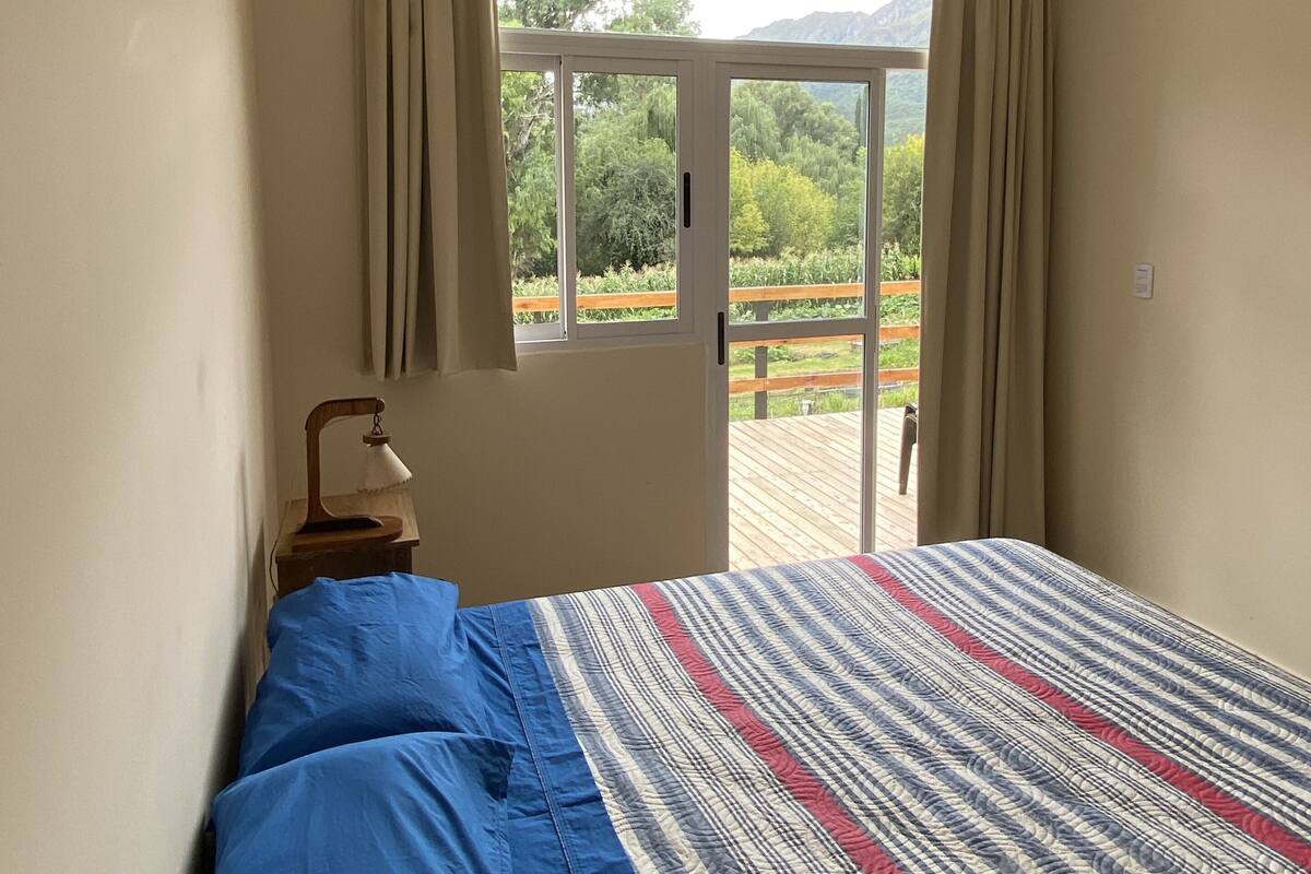 Une chambre à coucher avec un lit, une table de chevet, une lampe et une fenêtre avec des rideaux.