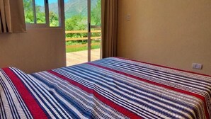 Una habitación con cama, ventana con cortinas y vistas a zonas verdes y montañas.