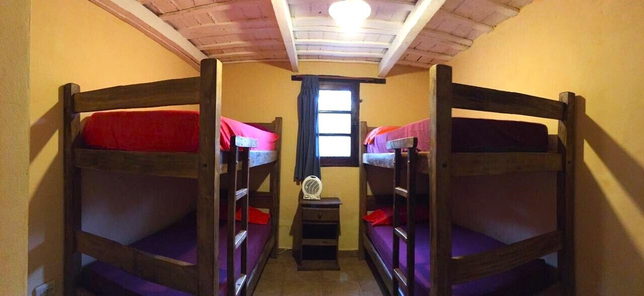 Una habitación pequeña con dos literas, una mesa y un ventanal con cortina.