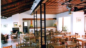 Un amplio comedor con mesas y sillas de madera, un techo alto con vigas a la vista y una chimenea.