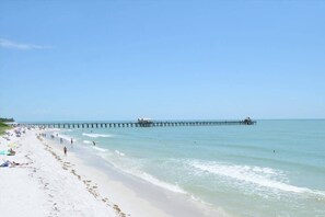 Una spiaggia con un molo che si protende nell'acqua, una riva sabbiosa e persone che passeggiano lungo la spiaggia.