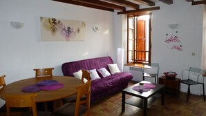 Un salón acogedor con un sofá púrpura, una mesa de comedor de madera y sillas. Hay una ventana con vistas al exterior.