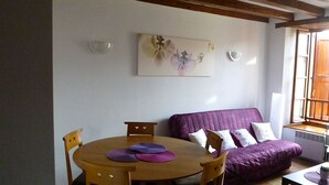 Una habitación con una mesa redonda de madera, un sofá púrpura y un cuadro en la pared.