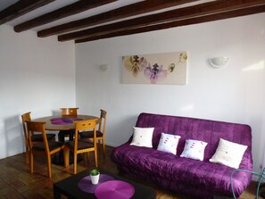 A room with a purple sofa, wooden dining table, and chairs.