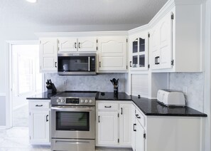 A modern kitchen with white cabinetry, a stainless steel range, a microwave, and a toaster.
