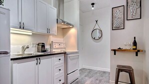 A kitchen with white cabinets, a stainless steel range hood, a coffee maker, and a wine bottle on a shelf. - A charming little apartment in the lower town (Québec)