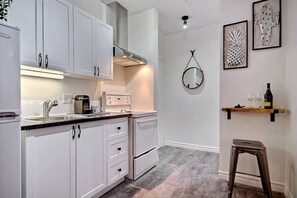 A kitchen with white cabinets, a stainless steel range hood, a coffee maker, and a wine bottle on a shelf. - A charming little apartment in the lower town (Québec)