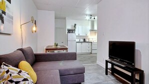 A living room with a gray sofa, a television on a stand, and a kitchen in the background. - A charming little apartment in the lower town (Québec)