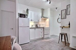 A modern kitchen with white cabinets, a microwave, and a stainless steel range hood. - A charming little apartment in the lower town (Québec)