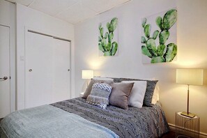 A bedroom with a bed, two wall-mounted paintings, a bedside lamp, and a door. - A charming little apartment in the lower town (Québec)