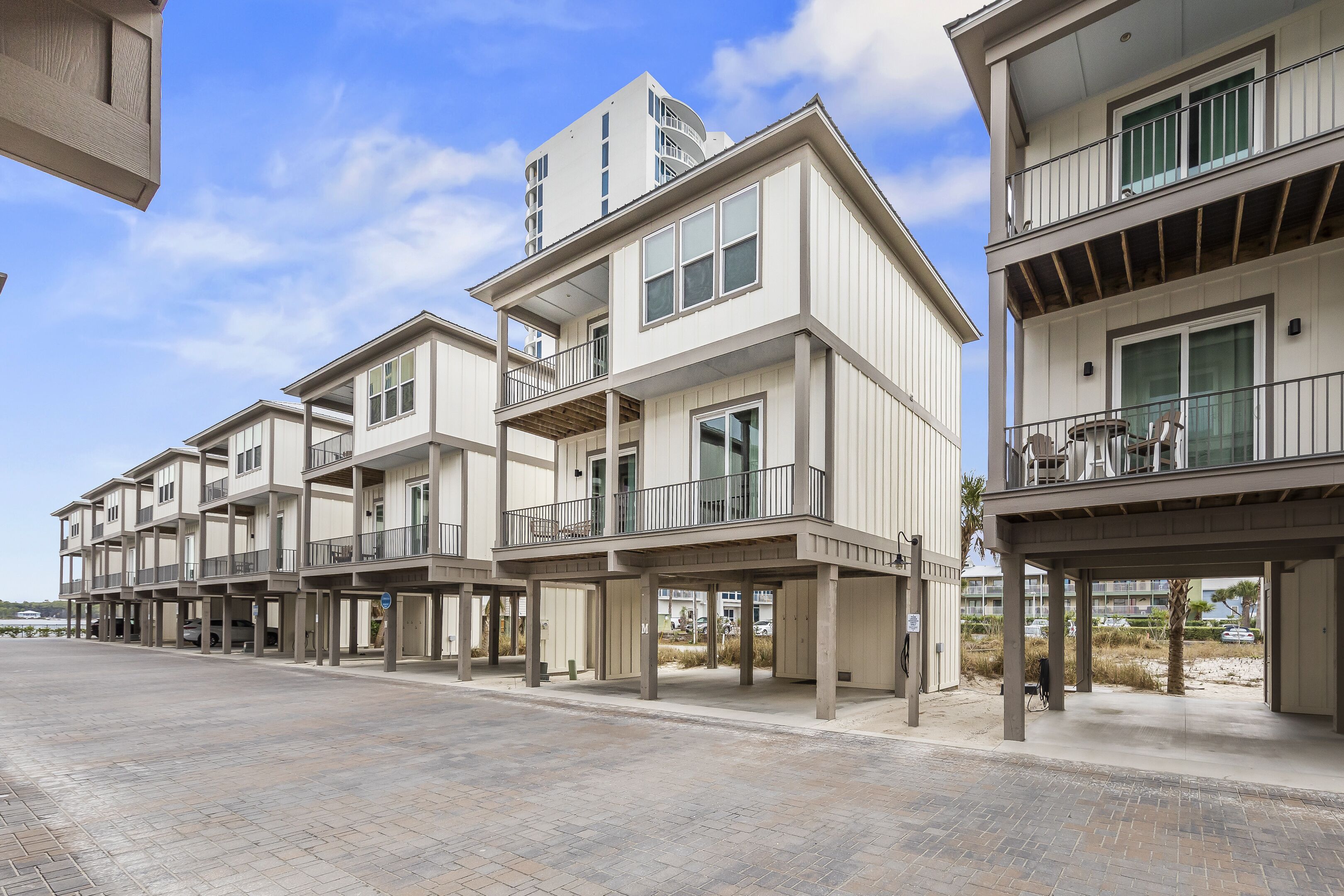 A row of modern multi-story buildings with balconies, a paved walkway, and a clear sky.