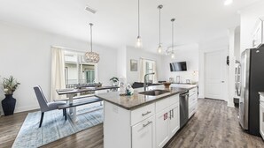 Een moderne keuken met een centraal kookeiland, witte kasten en een eethoek met tafel en stoelen.