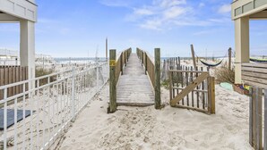 Een houten looppad dat naar een strandgedeelte leidt, met een witte omheining en een hangmat.