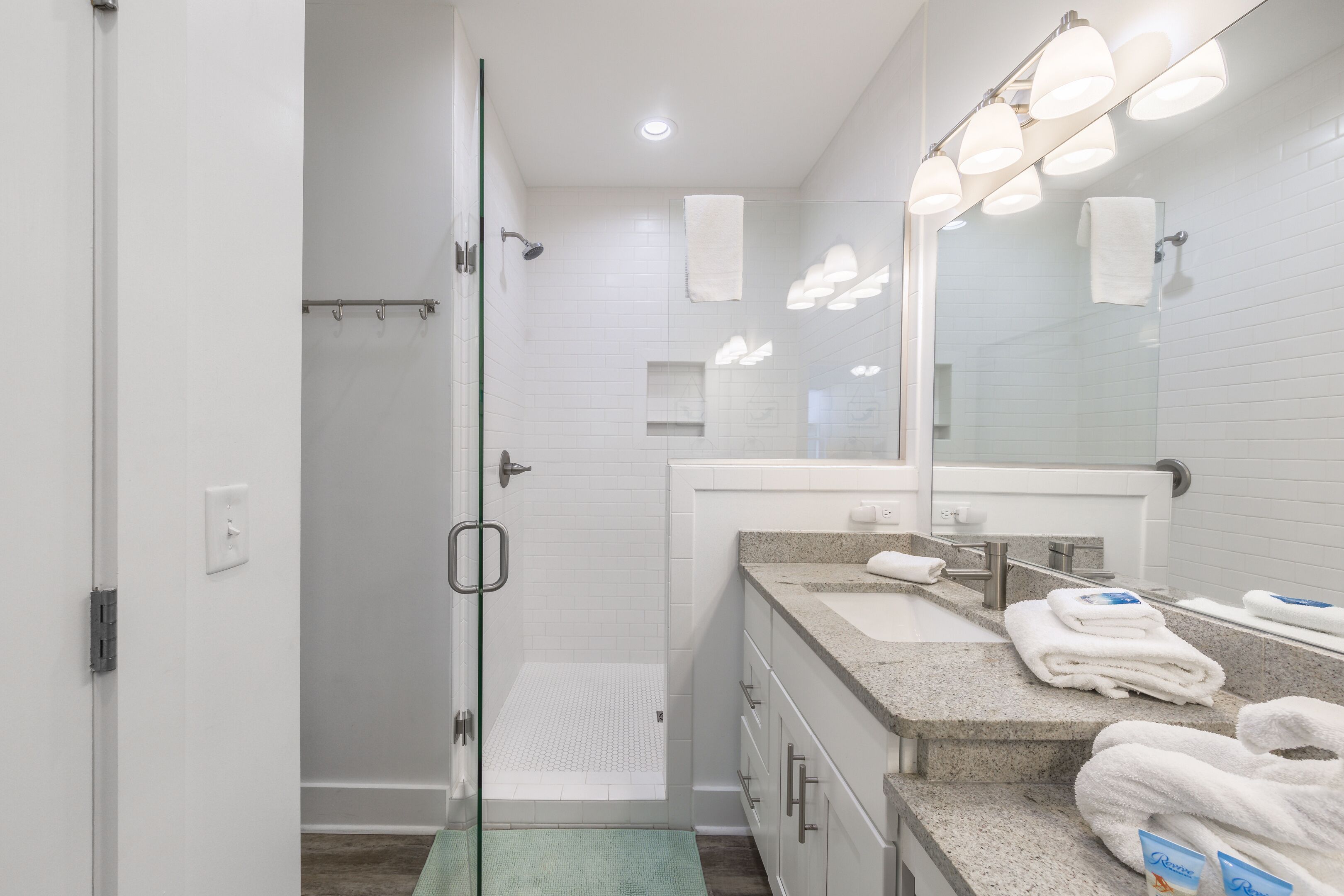 A modern bathroom with a glass shower door, a vanity with a sink, and a large mirror with lights.