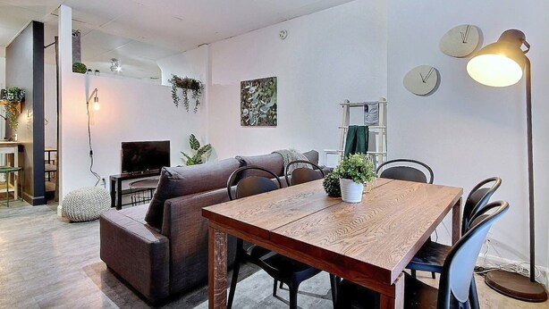 A modern living space with a wooden dining table, a sofa, and a TV.