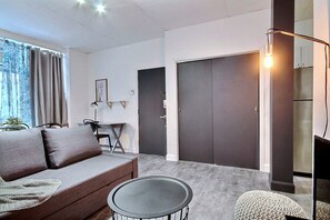 Uma sala de estar moderna com um sofá, uma mesa de centro redonda e uma luminária. Há duas portas e uma pequena mesa com cadeiras.
