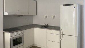 Et kompakt køkken med hvide skabe, indbygget ovn, køleskab og vask.