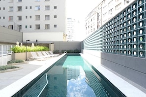 Piscina no terraço com espreguiçadeiras e vista para os edifícios ao redor.